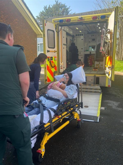 Image of a mum and baby with Community Midwife on an ambulance bed heading into the ambulance 