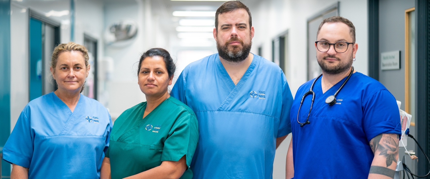 Four nursing staff members standing together in the corridor looking sad, one with her arms crossed and one with a stethoscope around his neck. 