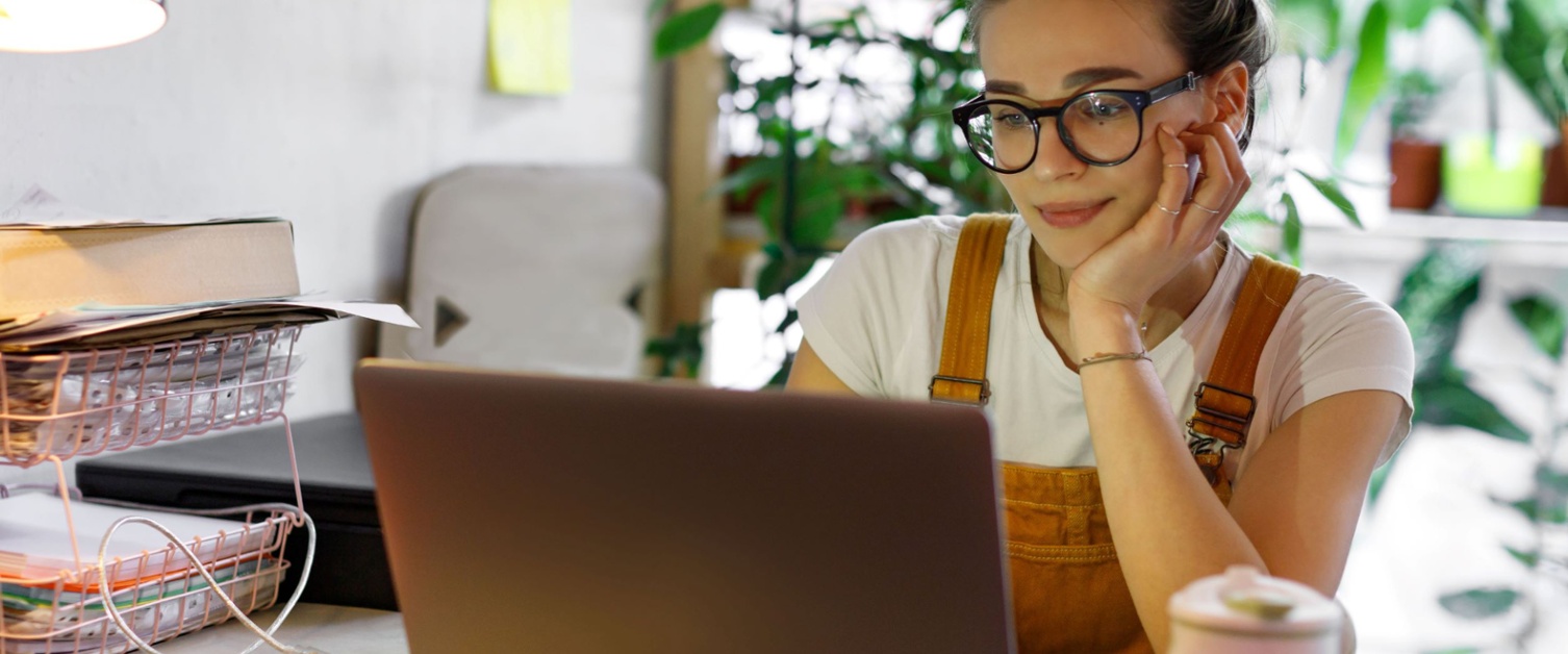 a young person wearing glasses, sitting at a desk using a laptop. 