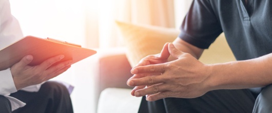 Doctor and patient sitting on a couch facing each other, having a conversation. 