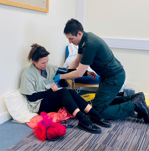 Llun o Paramedic yn gwirio pwysedd gwaed ar glaf.