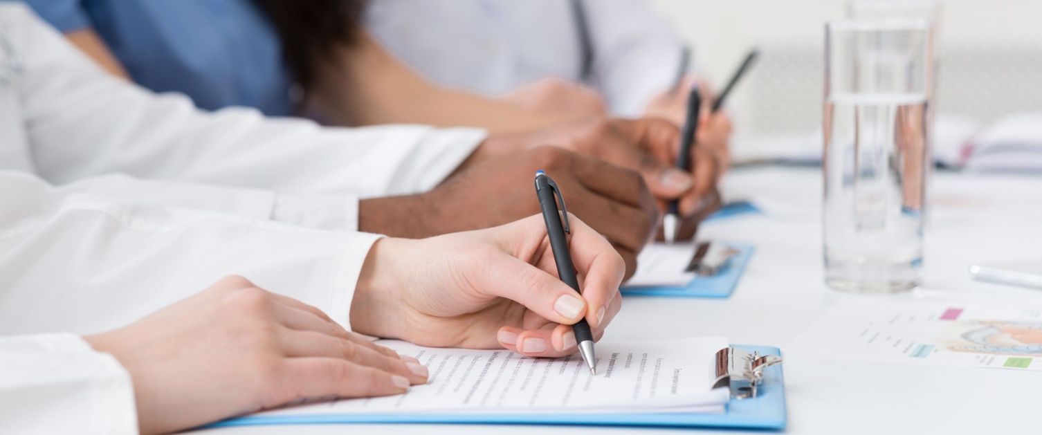 Trainee doctor writing on a clipboard on a desk. 