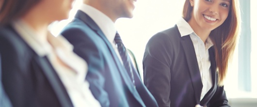 Business people in a meeting with a blonde haired woman looking into the camera and smiling. 