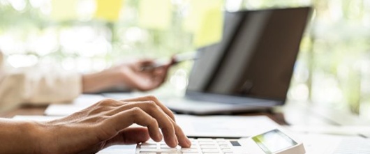 Person using a computer and a calculator on a desk. 