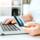 Person using their laptop while holding a credit card to indicate making a purchase. 