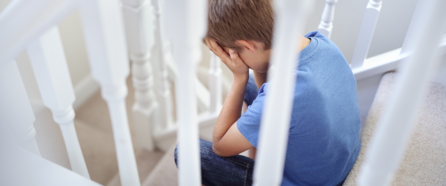 Young boy sat on stairs with head in hands