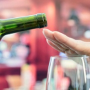 Image of hand over wine glass, while glass of wine being offered