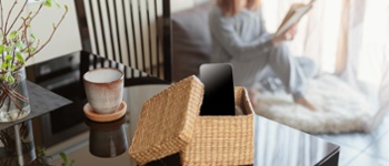 Woman sitting near window and reading book. Focus on box with smartphone. Digital detox and leisure concept