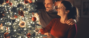 Image of couple bonding while decorating the glowing Christmas tree on cosy Christmas Eve.