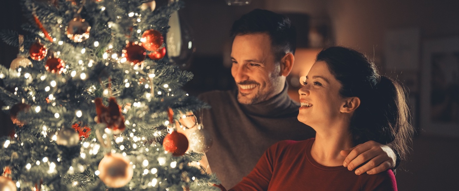 Image of couple bonding while decorating the glowing Christmas tree on cosy Christmas Eve.