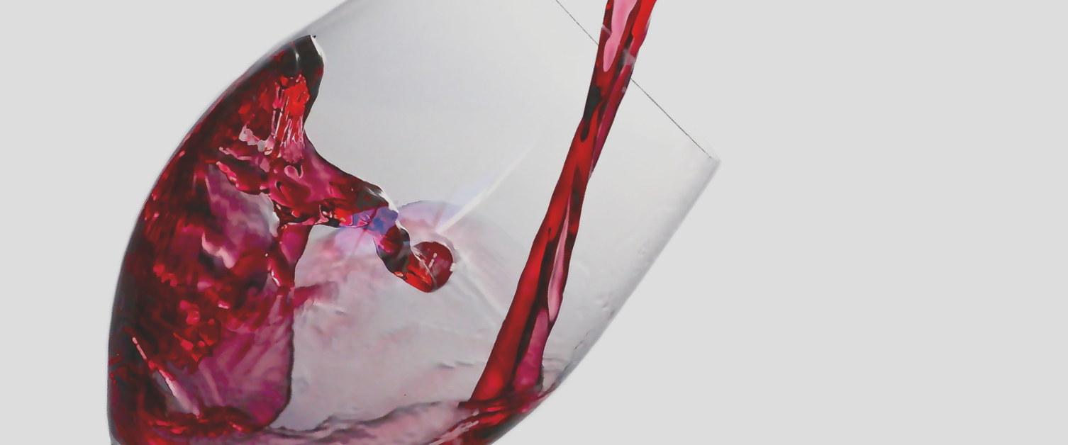 Close up image of red wine being poured in to a wine glass against a white background.