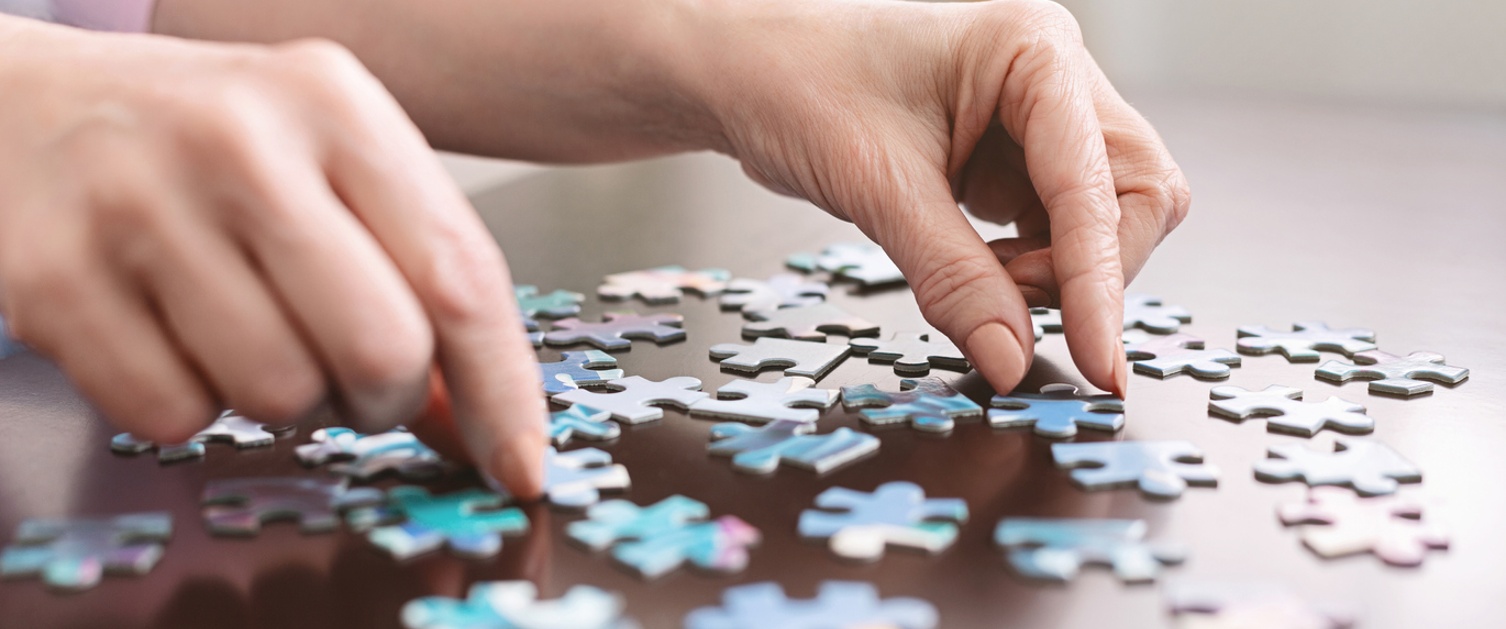 Dementia prevention. Elderly woman hands doing jigsaw puzzle at home, panorama, close up