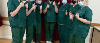 7 female apprentices wearing masks and green scrubs with their thumbs up