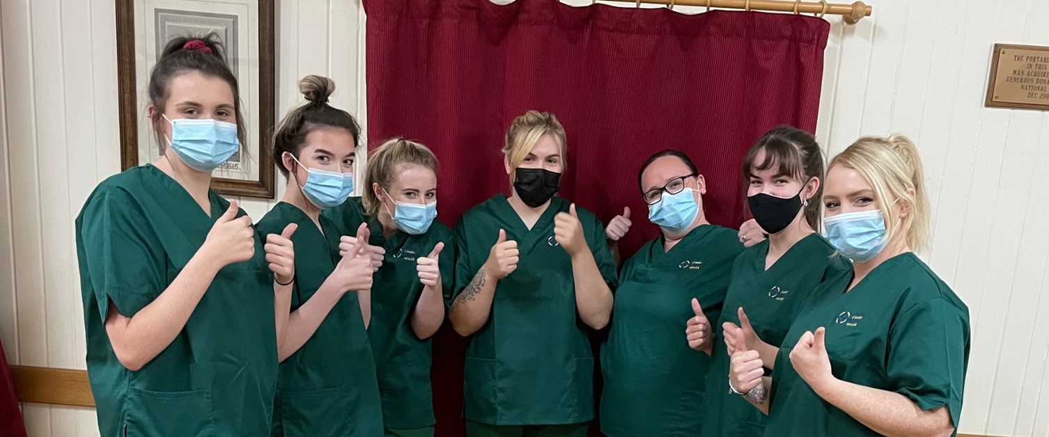 7 female apprentices wearing masks and green scrubs with their thumbs up