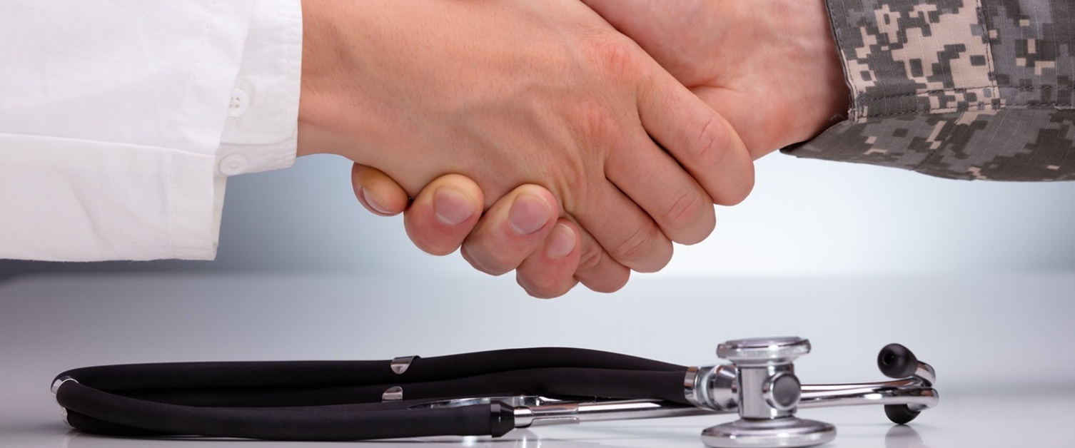 Doctor and a Military Man Shaking Hands Over the Stethoscope on White Table