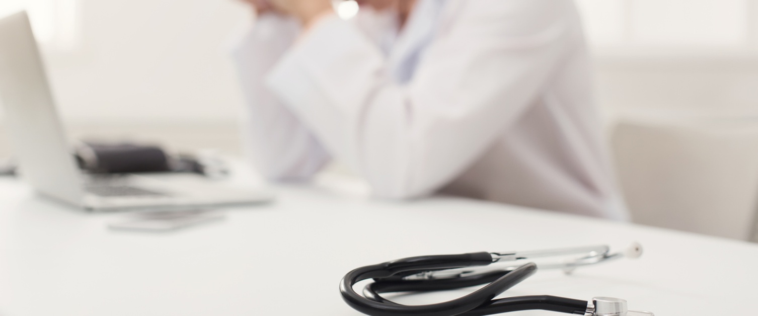 Tired doctor with head in hands sitting at workplace.