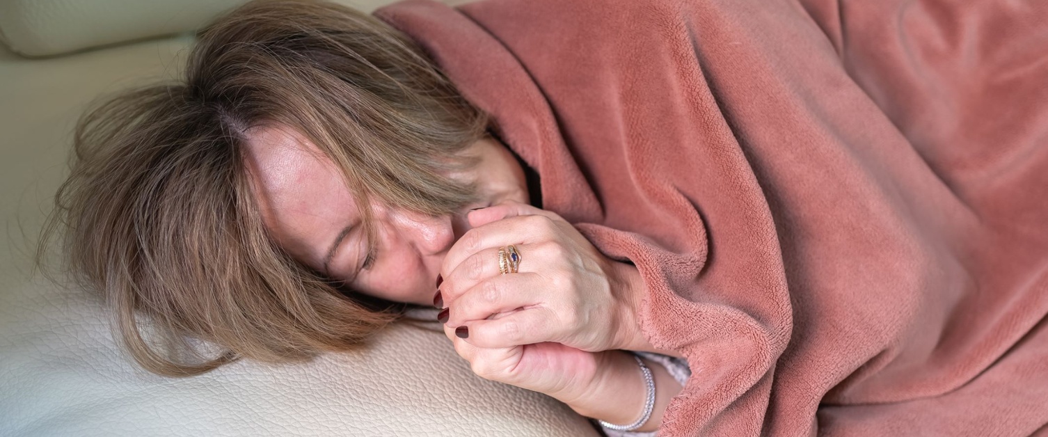 Woman lying on a sofa and going cold through the winter,blowing her hands to warm herself.