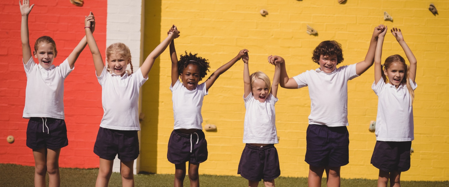 Happy school children standing with hand in hand in schoolyard