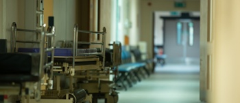 Copilot said:  English Alt Text  Hospital corridor with patient trolleys and seating lined along the hallway, leading towards double doors in the distance.