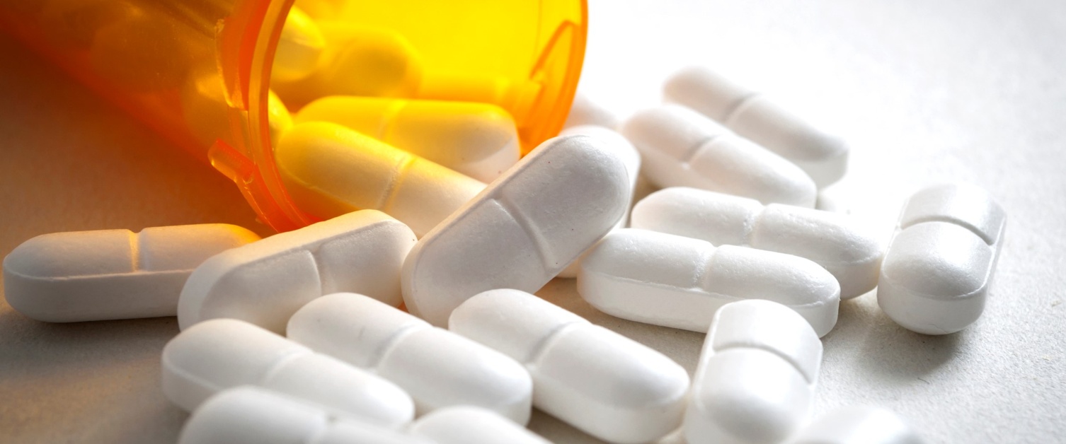 Close up on a bottle of prescription drugs and pills falling out of it on white surface