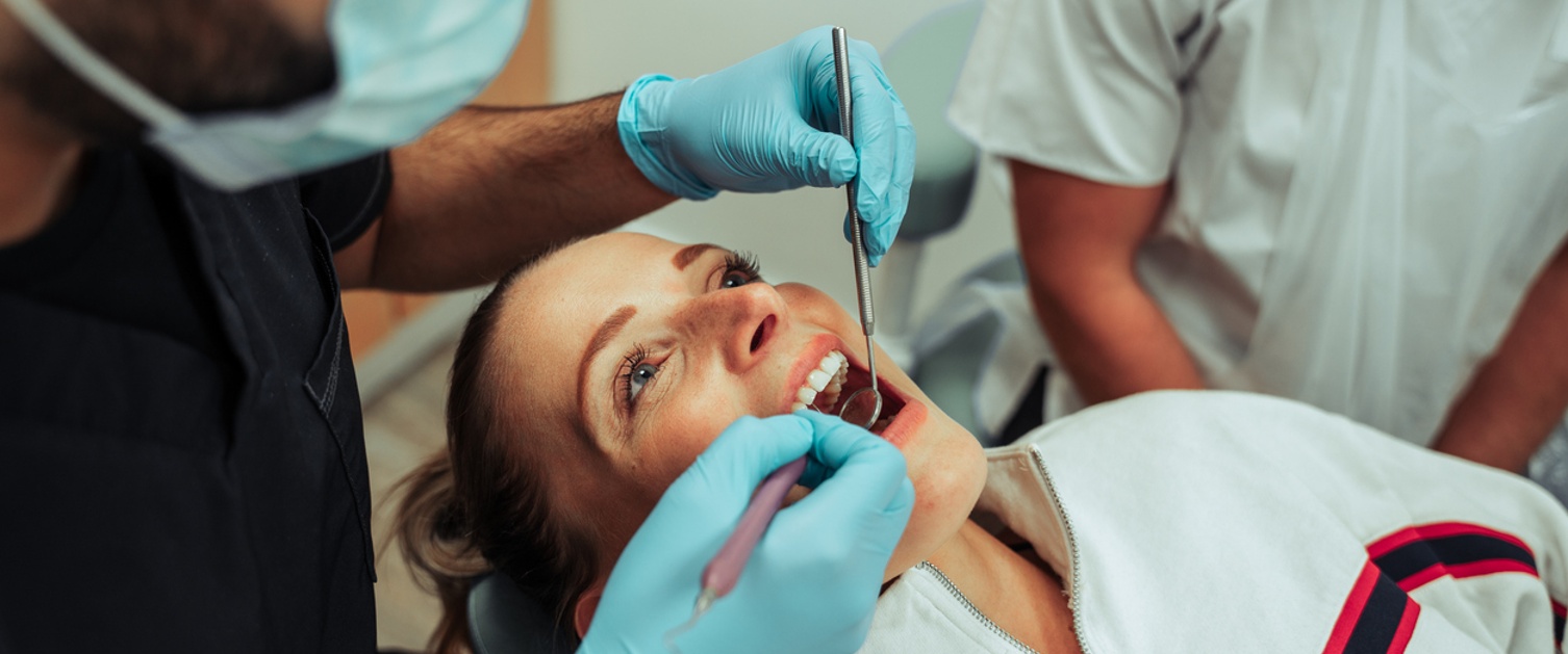 female patient lying with open wide mouth while male dentist operates on teeth
