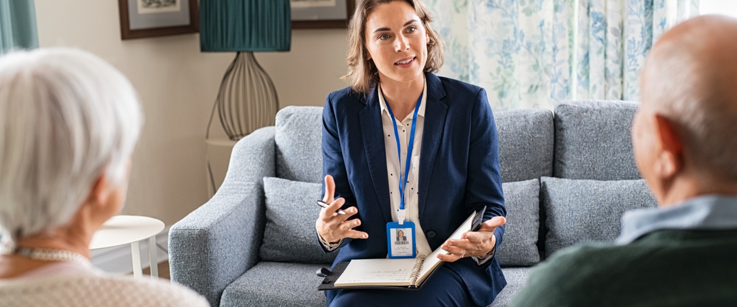 Woman support worker explaining medical details to senior couple at home