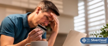 Image of male head in hand with bank card in other hand looking at laptop screen.