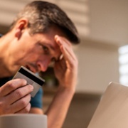 Image of male head in hand with bank card in other hand looking at laptop screen.