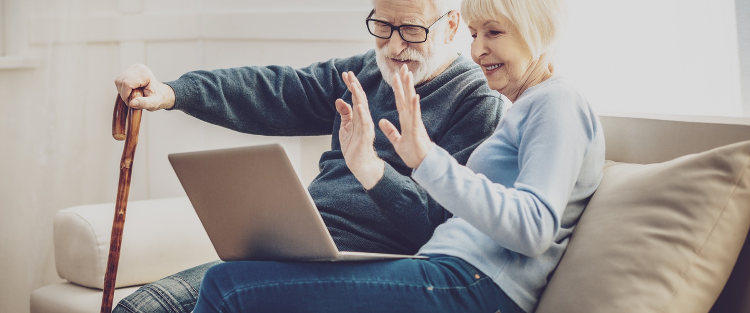 Older couple sat on sofa waving at laptop screen