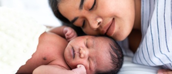 Image of mum hugging and kissing her newborn baby on white bed. Close up of infant with young mother