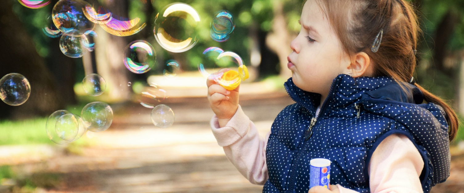 Pretty little girl blowing bubbles in the park