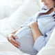 Pregnant woman in bed holding her stomach and smiling