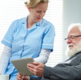 The image shows a member of clinical staff providing support to a patient using an iPad.