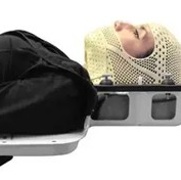 A person lying on a tray with a head covered in a mesh