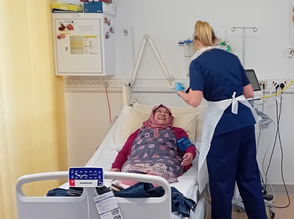 Farhana Badat lying on hospital bed with nurse Ruth Allan leaning over her to take her blood pressure