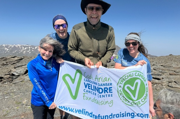 A group of people hold a 'Velindre Fundraising' flag on top of a mountain.