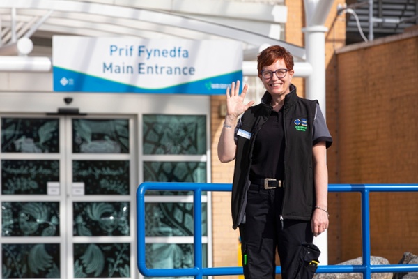 A person smiles and waves outside Velindre Cancer Centre.