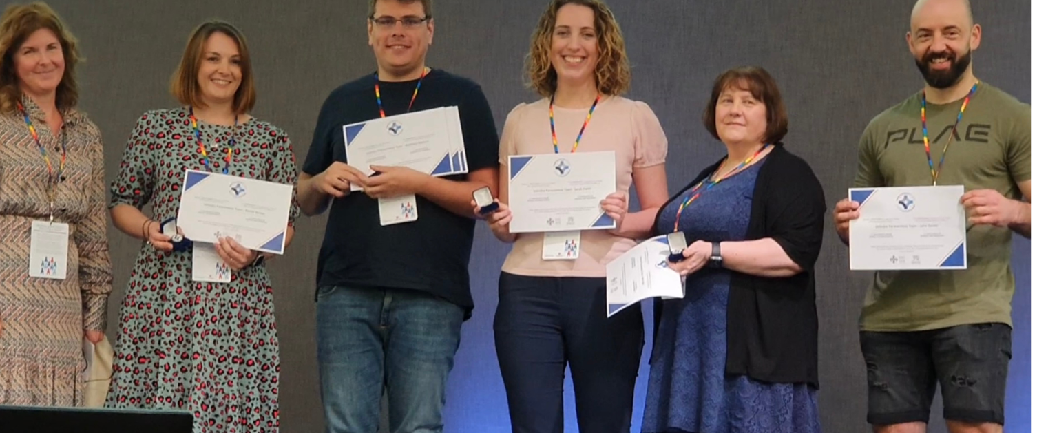 Six members of Velindre’s Paracentesis Service are smiling on stage with their award from the Chief Nursing Officer for Wales.