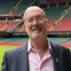 Professor Tom Crosby OBE stands on the pitch at the Principality Stadium. He is wearing a suit, smiling and happy.