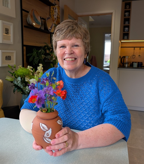 Gwen Buchan in blue top smiling holding a vase with flowers 