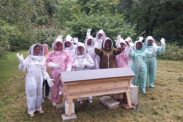 A group of bee keepers are in their kit and next to a bee hive.