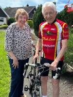 Two people are smiling in the sunshine. One is holding a bicycle.