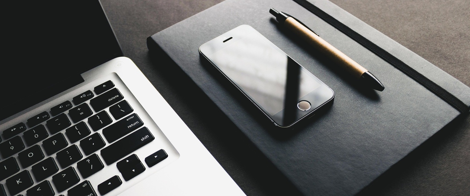 A stock image of a laptop, a mobile phone and a notepad and pen.