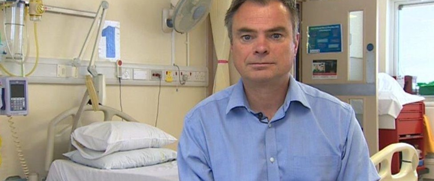 A person ina  blue shirt sits in a hospital room.