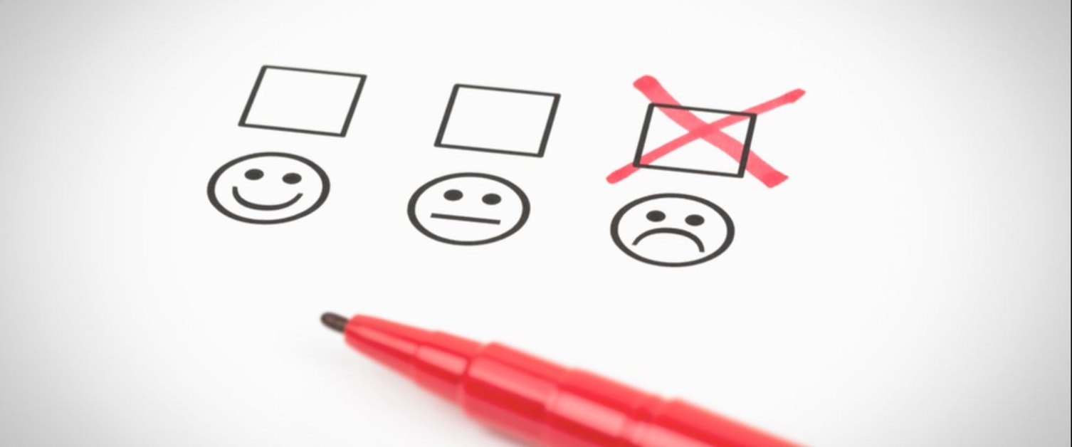 A form shows three faces. One is smiley, one is neutral and one is unhappy. A red pen has marked the unhappy face.