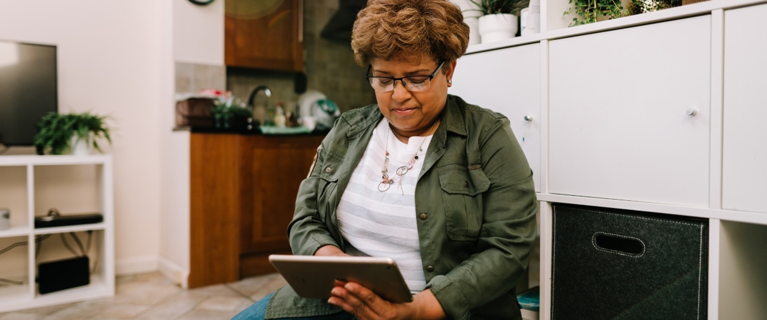 A lady is sat on a sofa and using a tablet device.