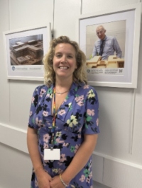 A woman is smiling and standing next to an art exhibition.