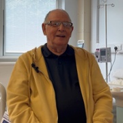 A man in a yellow jacket is smiling in a hospital ward.