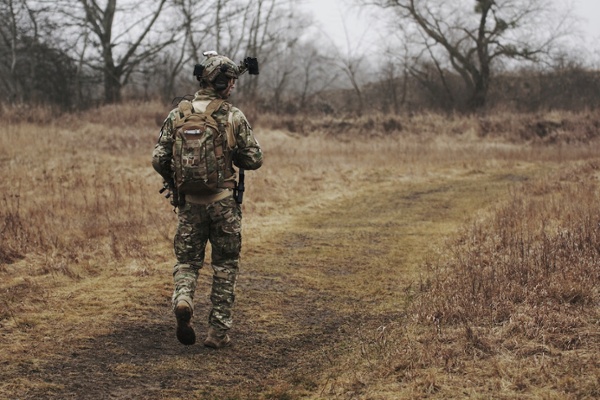 A uniformed soldier walks through a field.