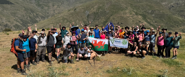 A large group of people are stood together on a mountian during a trek.